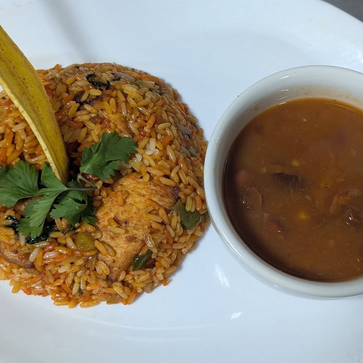 Arroz con pollo with a cup of beans and a pickle
