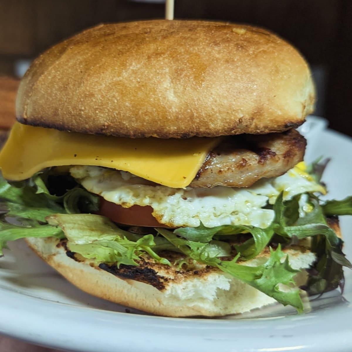 A breakfast sandwich on a toasted roll: egg, sausage, American cheese and greens