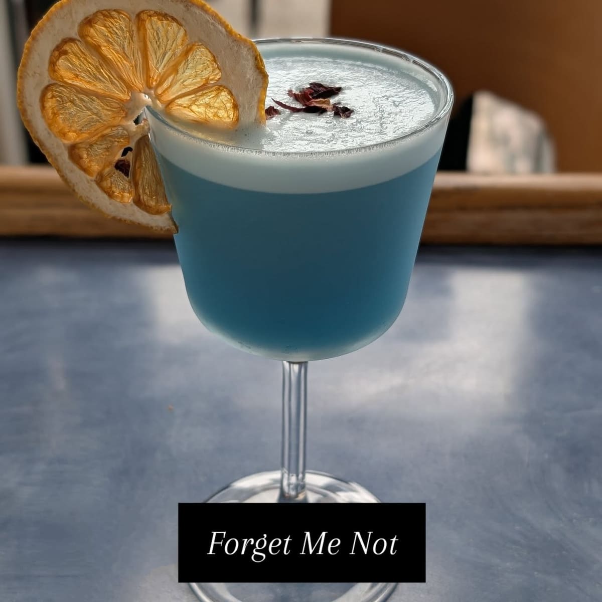 A pale blue cocktail in a coupe with a dried citrus wheel