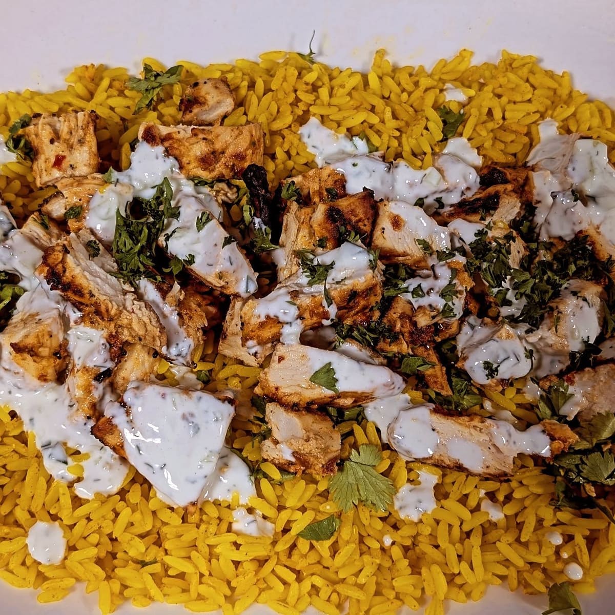 Grilled chicken over yellow rice with white sauce and herbs