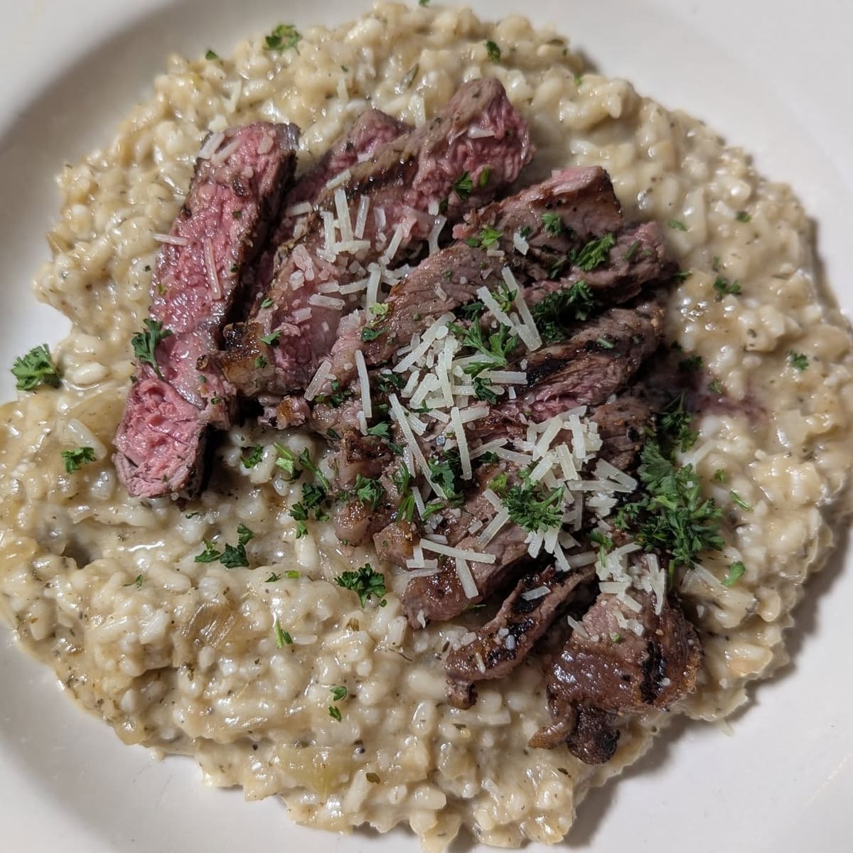 Sliced steak over risotto with parsley and shaved cheese
