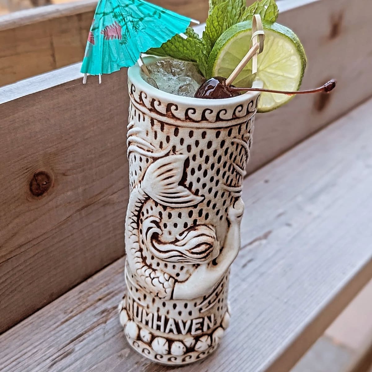Stroll punch in a carved tiki mug with a paper umbrella and lime